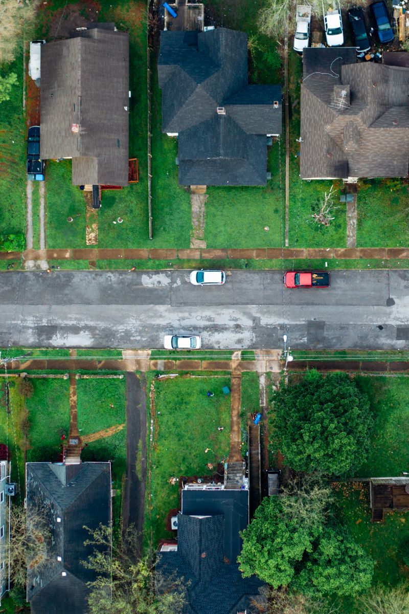 High-angle aerial shot of a suburban neighborhood street lined with houses and cars.