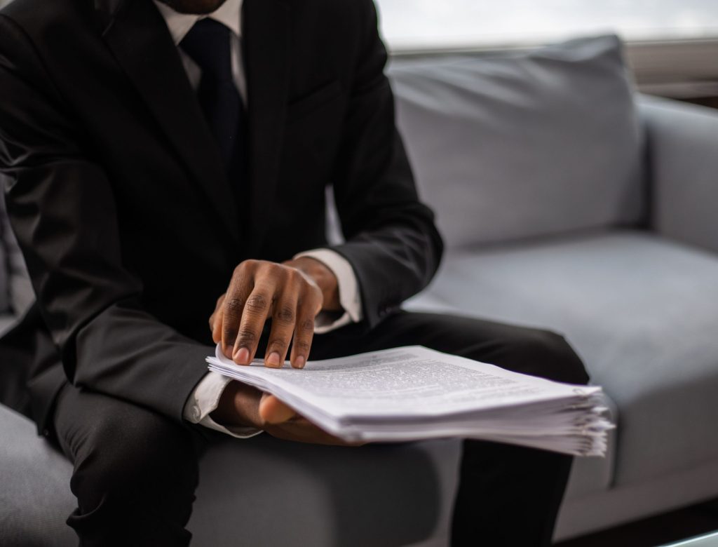 Close-up of a businessman in a suit reviewing documents while seated on a sofa indoors.